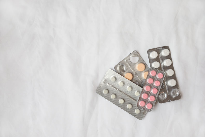 Variety of pills in silver blisters lie on white crumpled bed sh